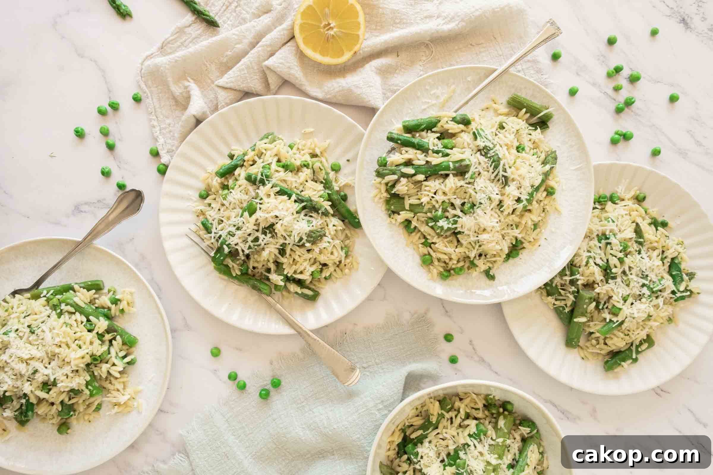 Plates of orzo with peas and asparagus on a counter beside half a lemon.