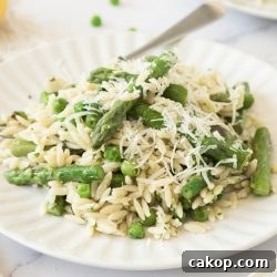 Plate of orzo with peas and asparagus garnished with grated Parmesan cheese.