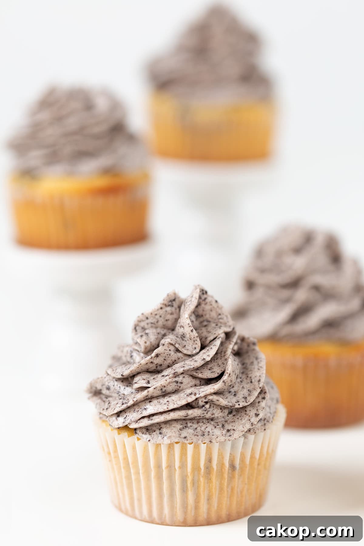 Cookies and Cream Cupcakes Recipe: Rich Oreo-Style Cupcakes 11 Four Oreo Cookies and Cream Cupcakes with rich cookies and cream frosting, displayed on a white surface, with two elevated on white stands in the background.