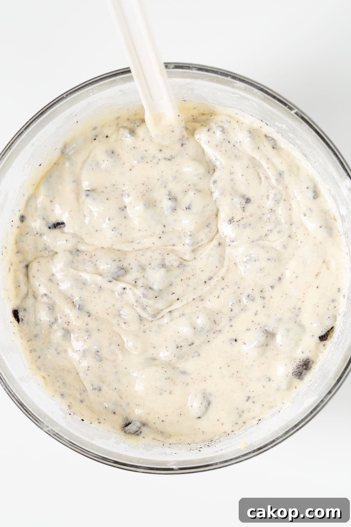 Cookies and Cream Cupcakes Recipe: Rich Oreo-Style Cupcakes 7 A glass bowl filled with a creamy, speckled Oreo Cookies and Cream Cupcakes batter is being mixed with a spatula.