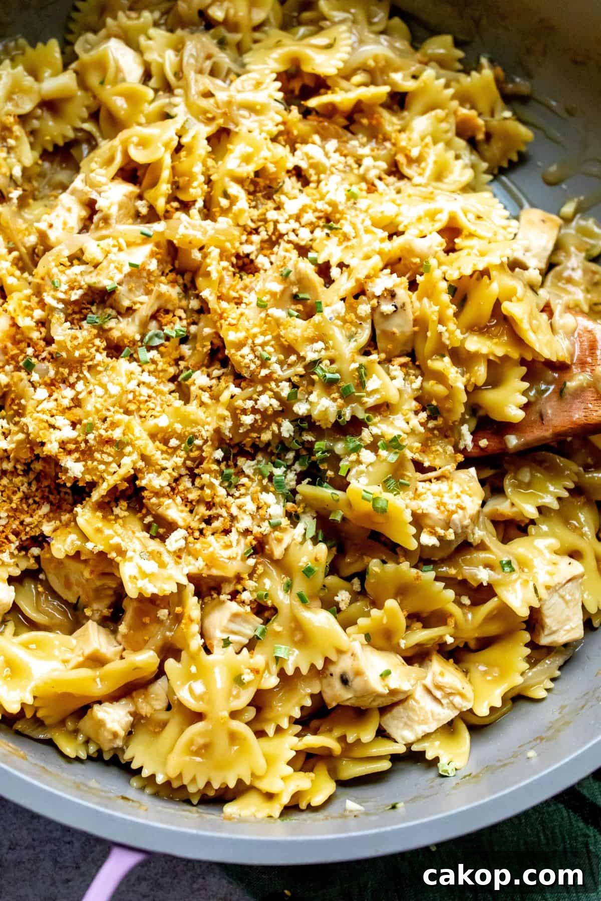 French Onion Pasta Recipe: Creamy Caramelized Onion Noodle Bake 5 Up close photo of grey and pink skillet with French Onion Pasta in it and a wooden spoon.