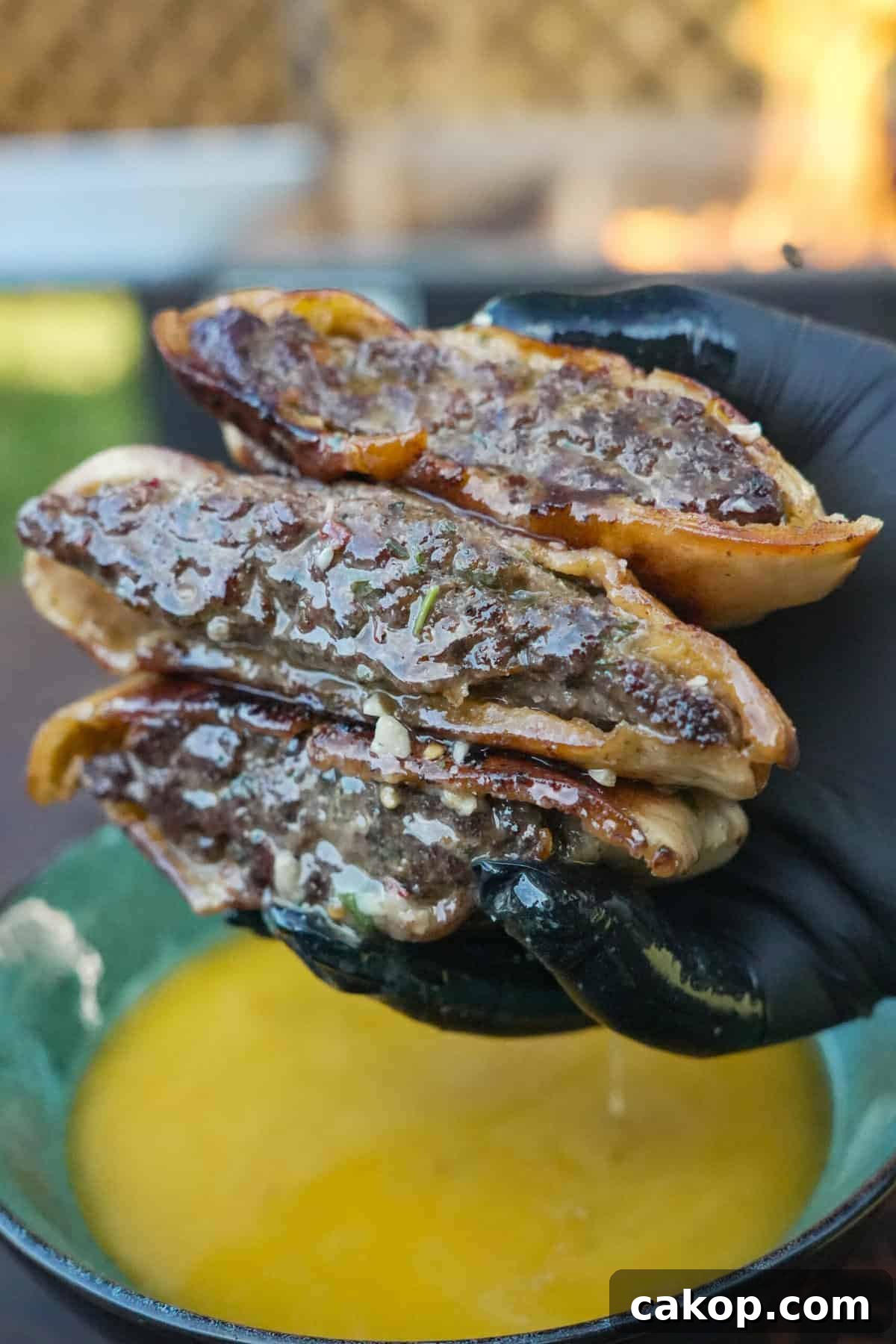 A gloved hand holding a stack of steak arayes over a bowl of cowboy butter