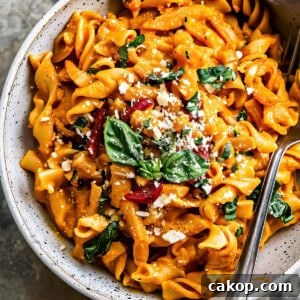 Roasted red pepper pasta with green and parmesan cheese in a bowl.