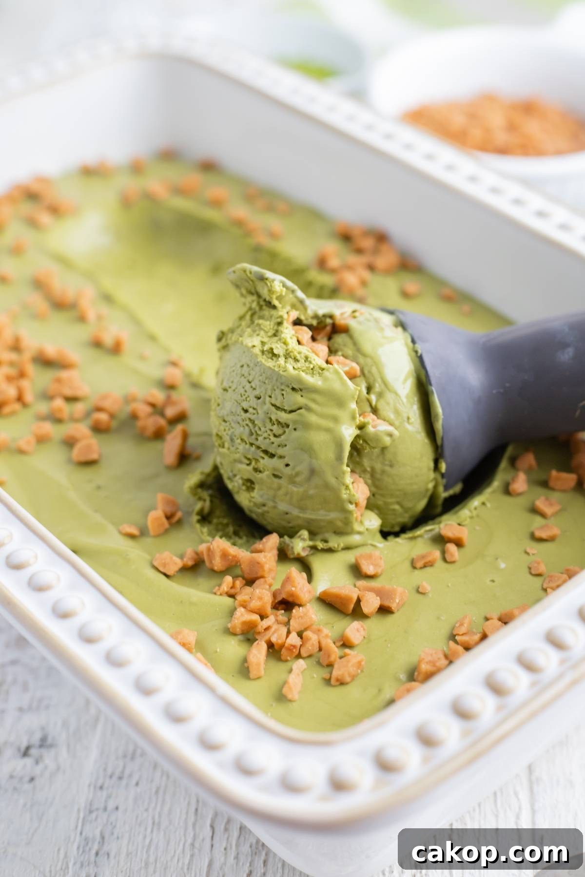 No-Churn Matcha Dulce de Leche Ice Cream Recipe 11 A scoop of green tea ice cream with toffee bits—this No Churn Matcha Dulce de Leche Ice Cream recipe is served in a white dish on a wooden surface.
