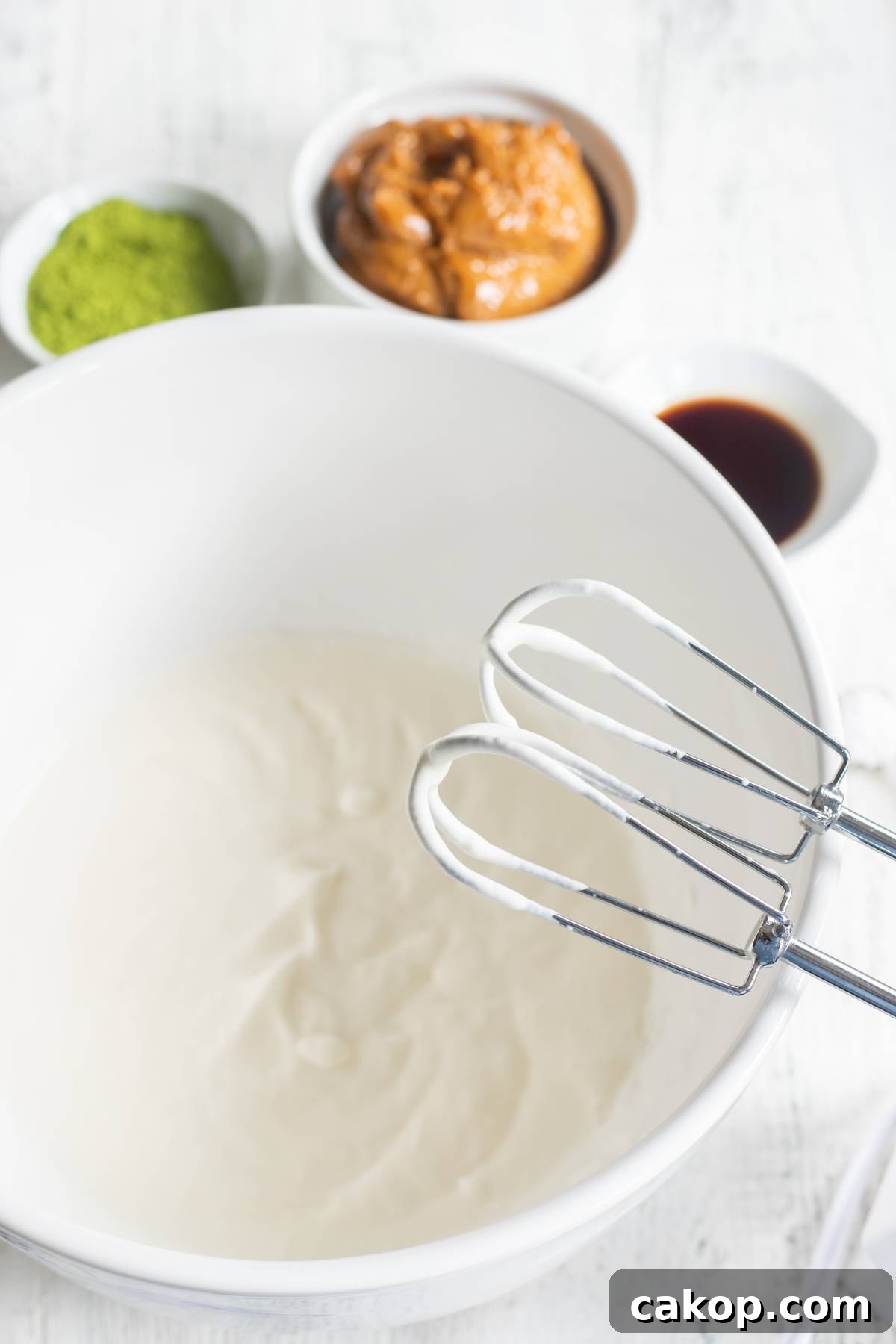 No-Churn Matcha Dulce de Leche Ice Cream Recipe 14 A bowl of whipped cream with electric beaters sits ready to become a creamy green tea ice cream, with matcha powder, peanut butter, and vanilla nearby for this easy no churn ice cream recipe.