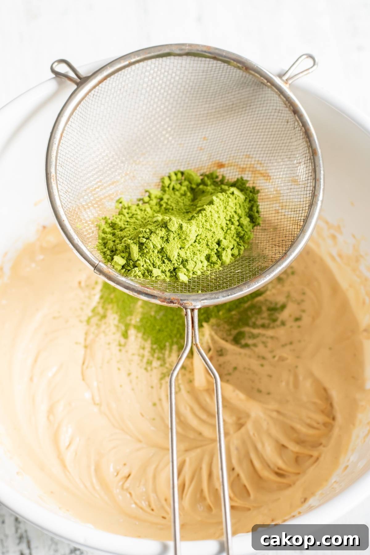 No-Churn Matcha Dulce de Leche Ice Cream Recipe 15 A sifter with green matcha powder over a bowl of light brown batter, perfect for making No Churn Matcha Dulce de Leche Ice Cream or any matcha ice cream recipe without a machine.