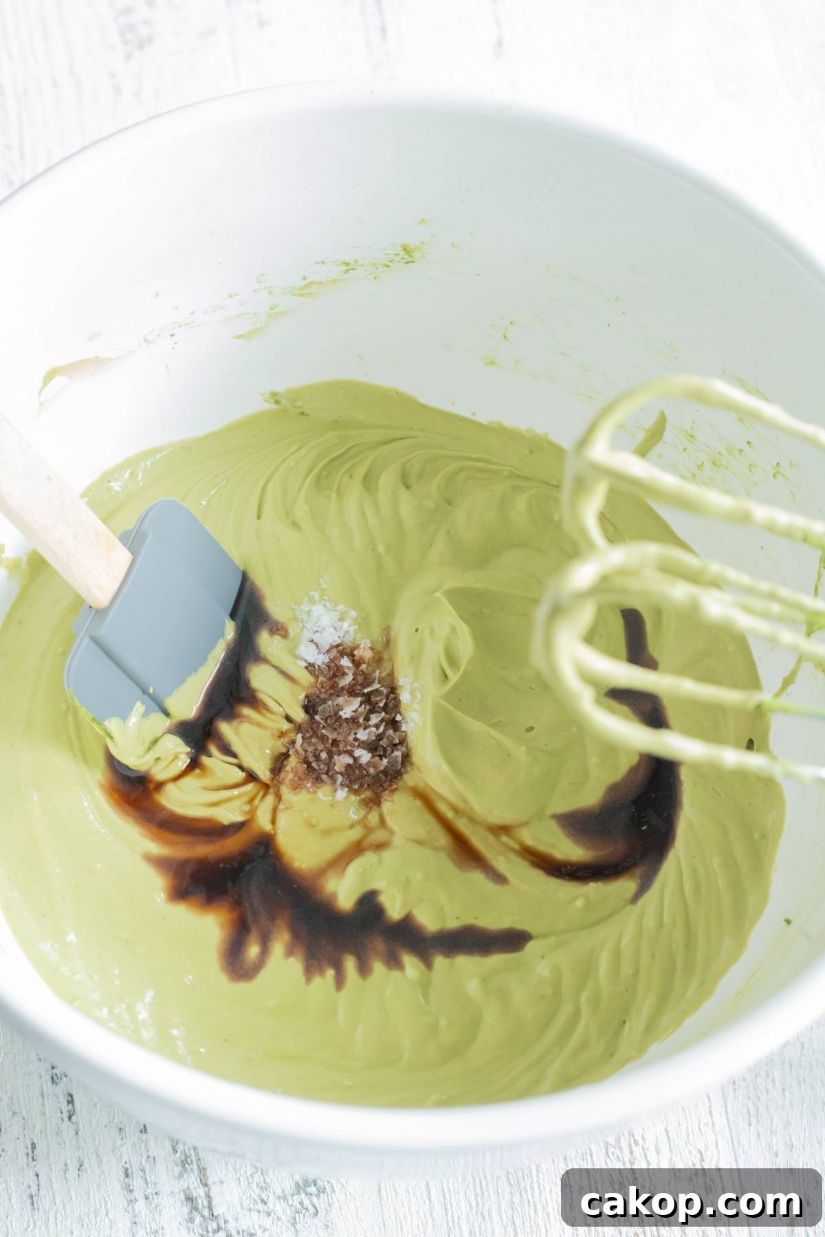 No-Churn Matcha Dulce de Leche Ice Cream Recipe 16 A mixing bowl with green batter, vanilla extract, salt, a spatula, and electric mixer beaters—perfect for making green tea ice cream or trying a No Churn Matcha Dulce de Leche Ice Cream recipe.