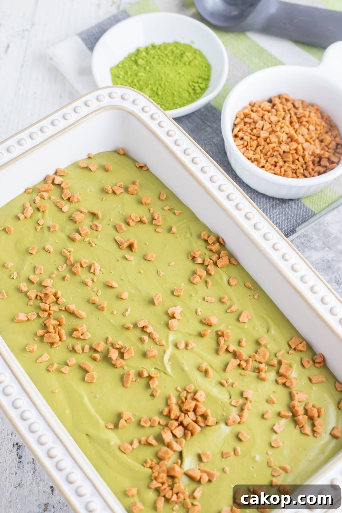 No-Churn Matcha Dulce de Leche Ice Cream Recipe 18 A white dish of green tea ice cream topped with toffee bits, with bowls of matcha powder and toffee nearby—an easy matcha ice cream recipe without a machine.