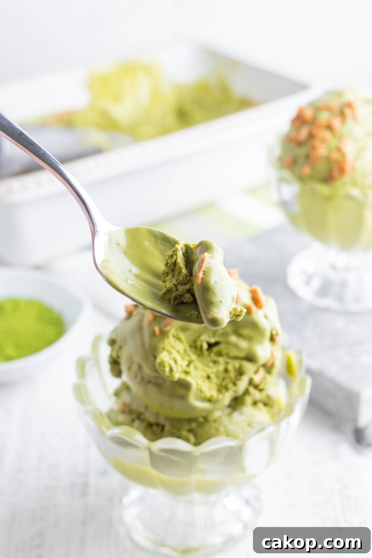 No-Churn Matcha Dulce de Leche Ice Cream Recipe 4 Spoonful of green tea ice cream above a glass bowl filled with more matcha ice cream—an easy matcha ice cream recipe without a machine.