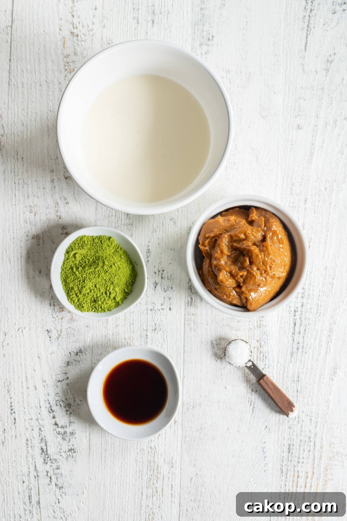 No-Churn Matcha Dulce de Leche Ice Cream Recipe 5 Four bowls with milk, peanut butter, matcha powder, vanilla, and a measuring spoon of salt on a white table—perfect ingredients for a matcha ice cream recipe without a machine.