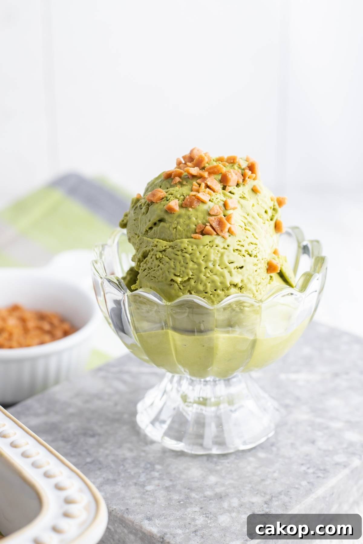 No-Churn Matcha Dulce de Leche Ice Cream Recipe 9 No Churn Matcha Dulce de Leche Ice Cream in a glass bowl, topped with chopped nuts, sits on a gray surface with a blurred background—a delightful recipe using Dulce de Leche.