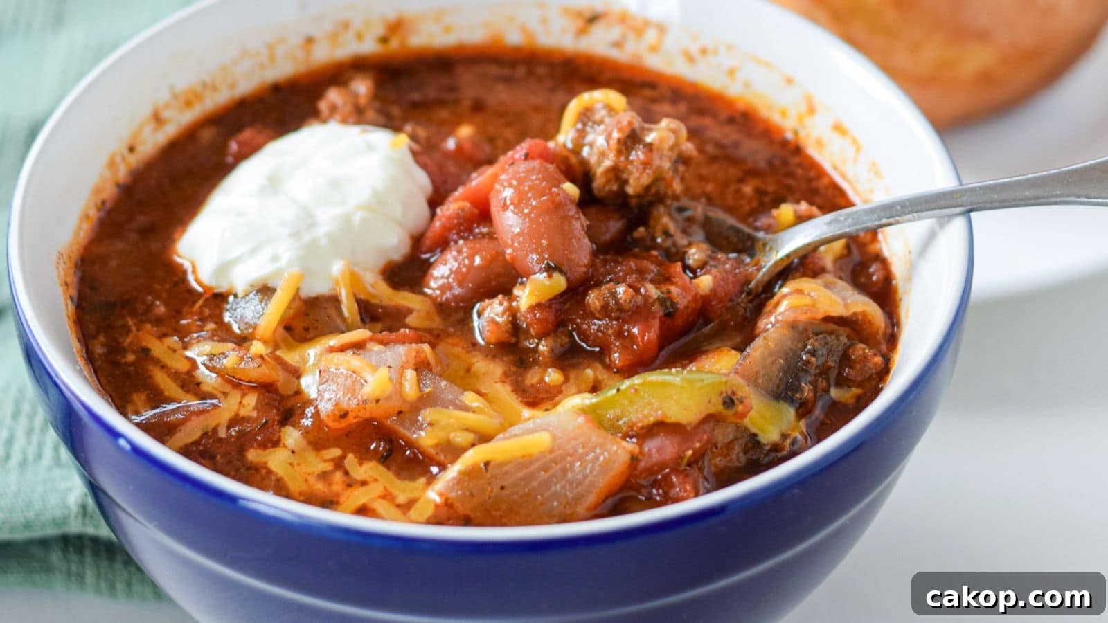 a blue bowl with chili in it, along with cheese and a dollop of sour cream