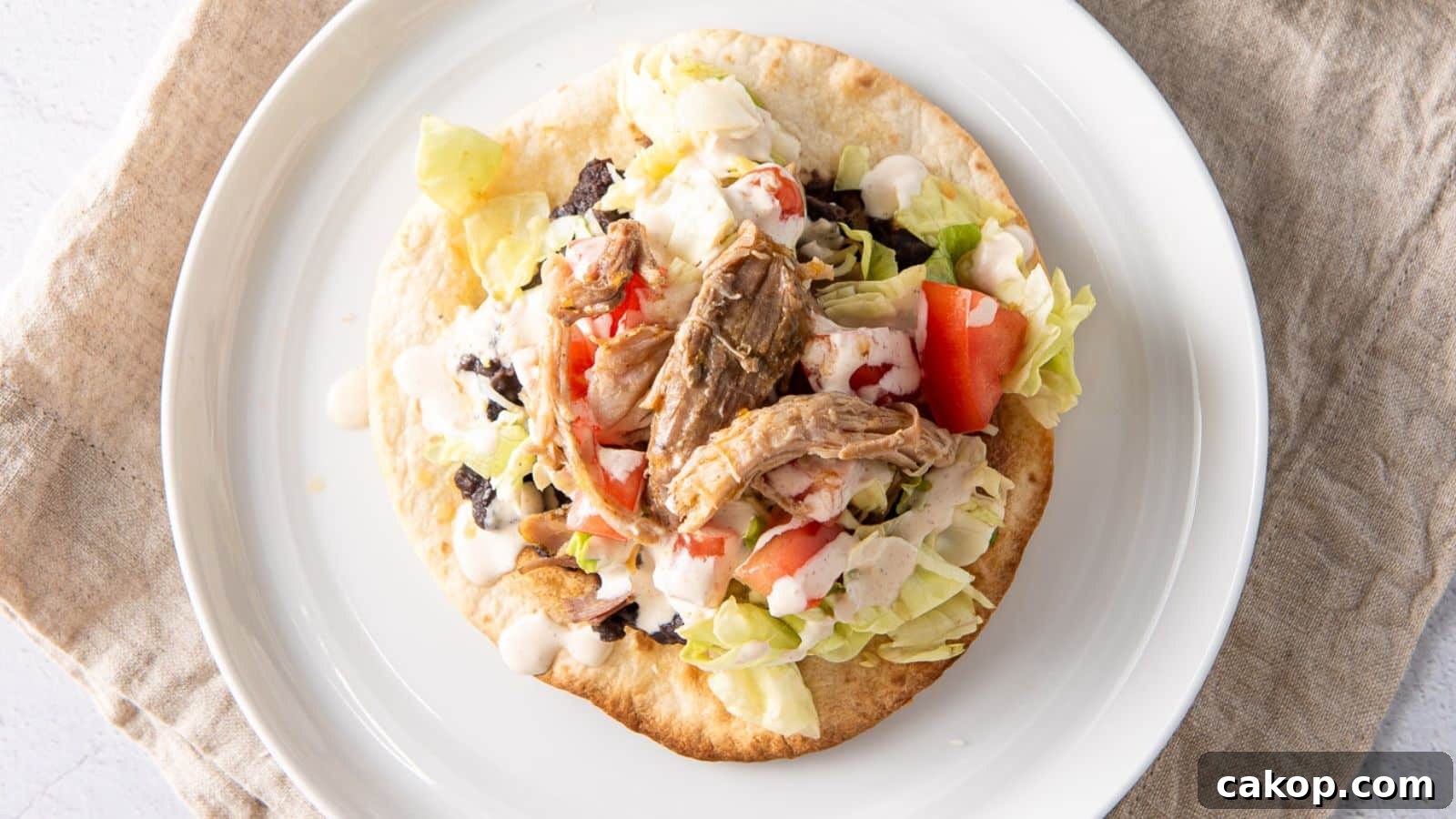 Overhead view of a crispy tortilla covered with lettuce, tomatoes, beans, a sauce and pulled pork