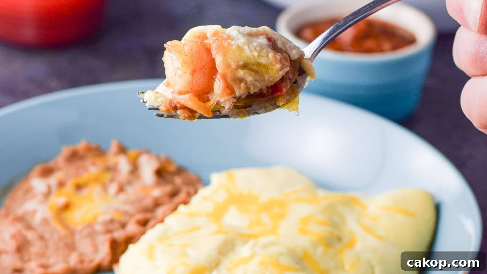 a hand holding a fork filled with the shrimp held over the plate of enchiladas and beans
