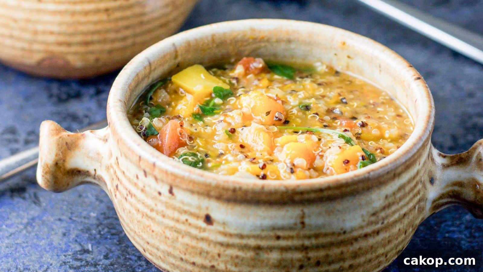 A crock with two handles filled with a stew with squash, quinoa, and more vegetables