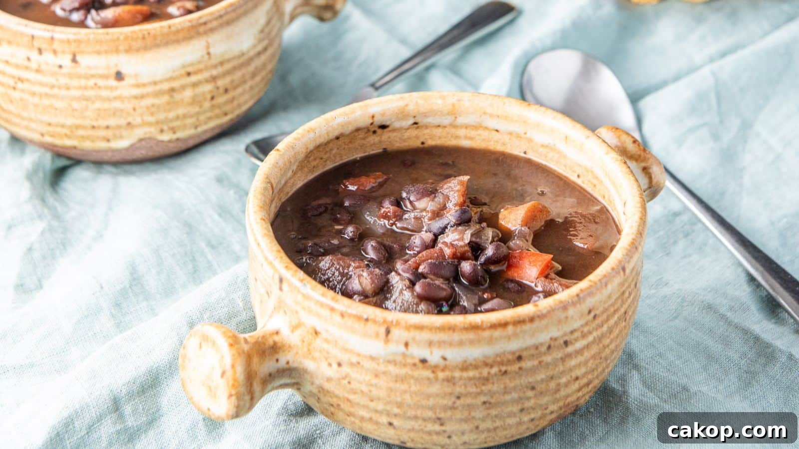 Black beans and carrots soup in a crock with two spoons on a green napkin