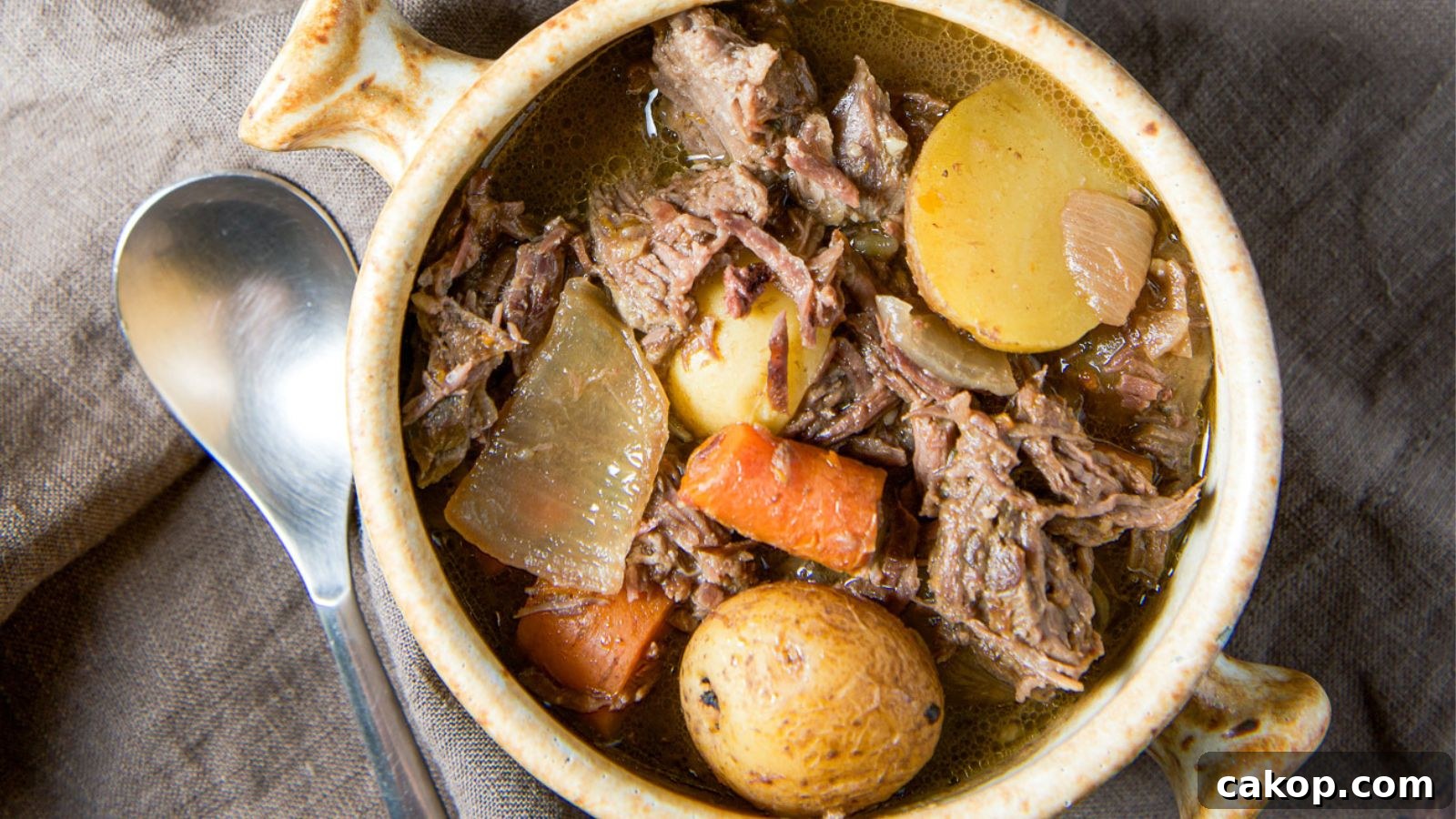 an overhead view of potatoes, carrots and beef pot roast in a bowl with a spoon