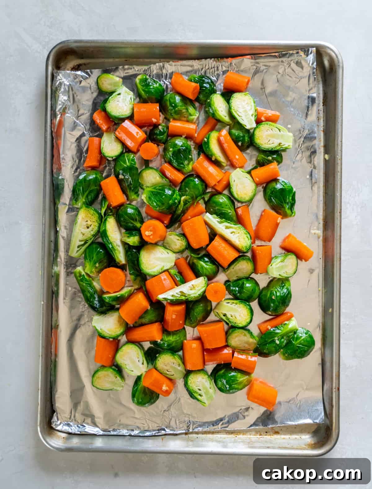 Brussels sprouts and carrots on a sheet pan with olive oil, garlic, salt, pepper, and red pepper flakes. The pan is sitting on a white countertop before going into the oven.