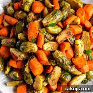 A large white bowl filled with roasted brussels sprouts and carrots sitting on a white countertop.