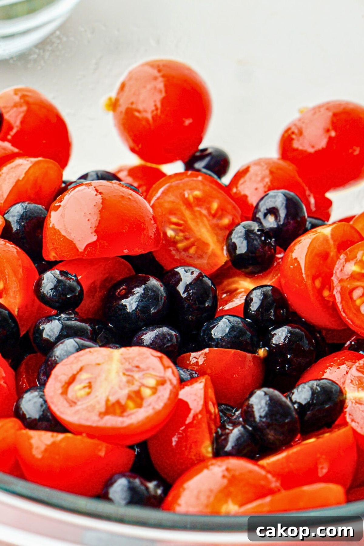 Berry Caprese Salad with Fresh Mozzarella and Balsamic 5 Blueberries and cherry tomatoes in a clear glass bowl tossed with oil and balsamic vinegar.