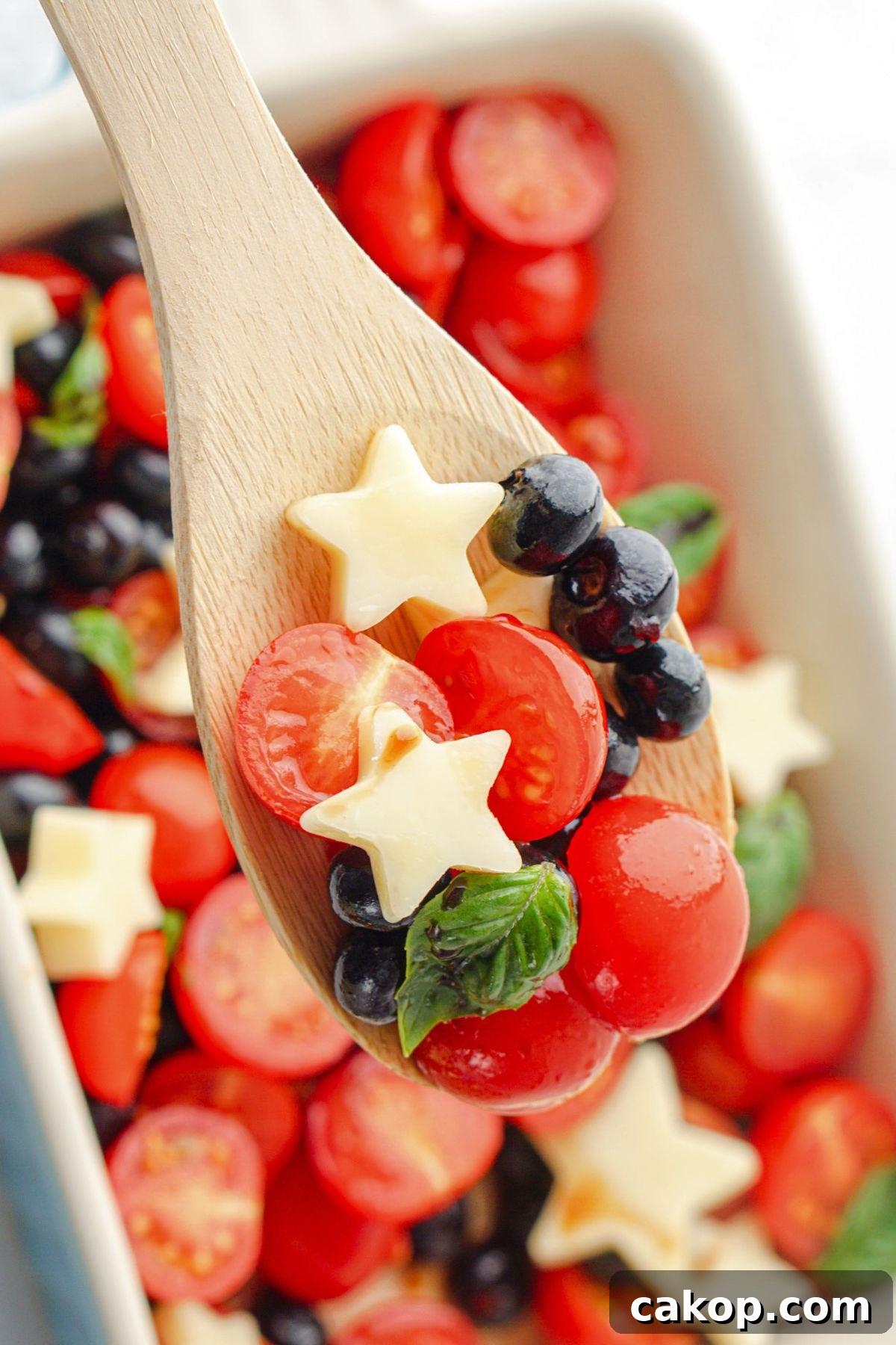 Berry Caprese Salad with Fresh Mozzarella and Balsamic 8 Spoonful of berries, tomatoes, and stars on a wooden spoon.