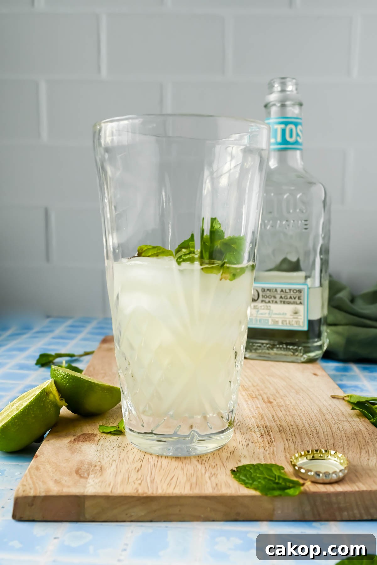 cocktail shaker filled with ginger beer, mint, tequila and ice on wood cutting board.