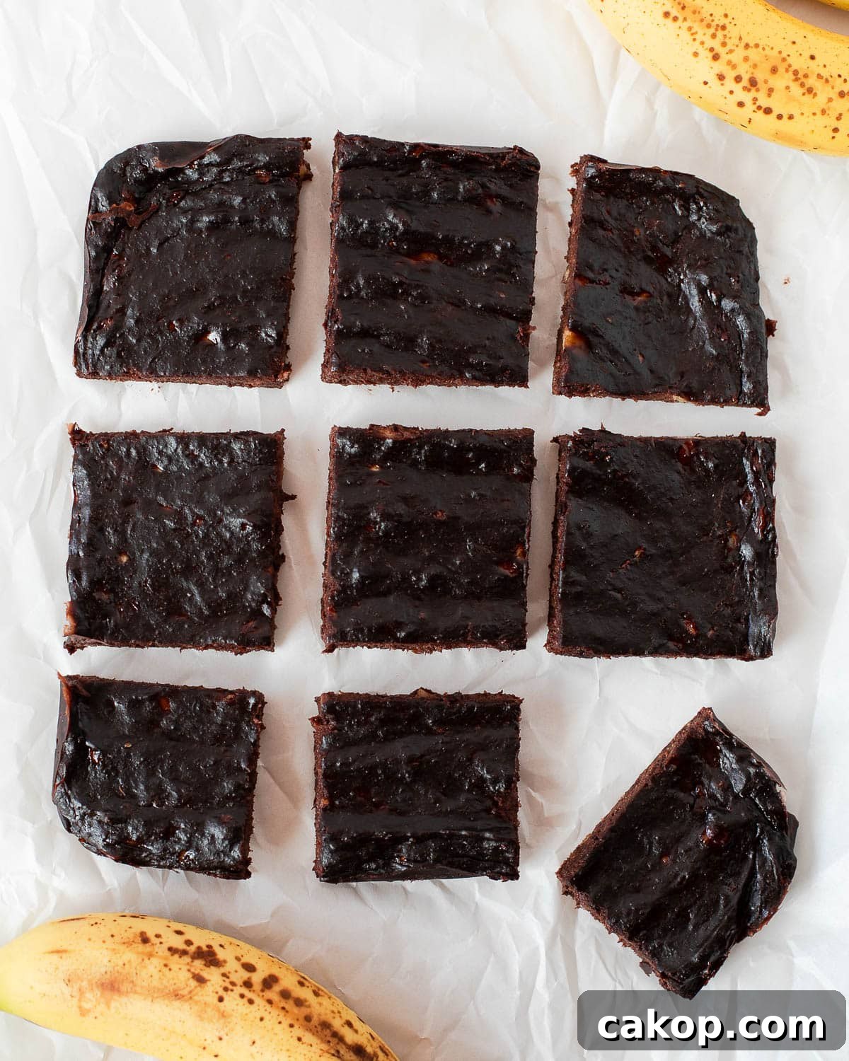 Overhead view of sliced 3 ingredient banana brownies arranged on parchment paper with ripe bananas.