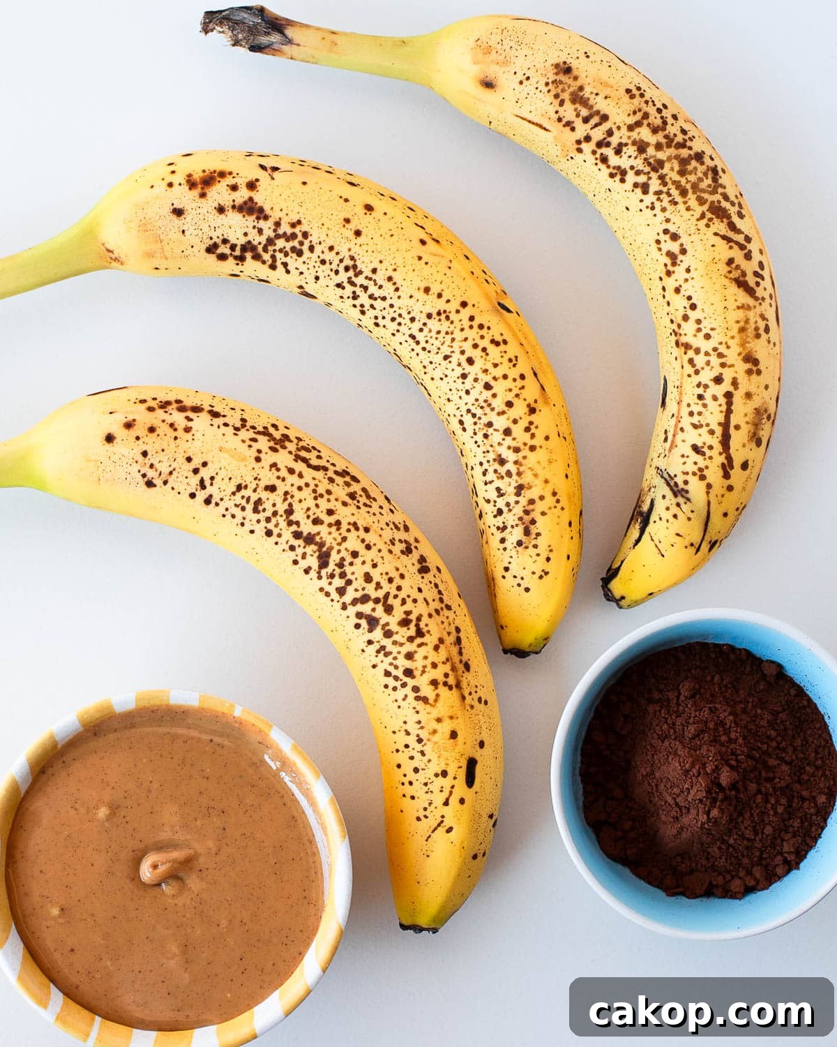 Overripe bananas, peanut butter, and cocoa powder arranged as ingredients for 3 ingredient banana brownies.