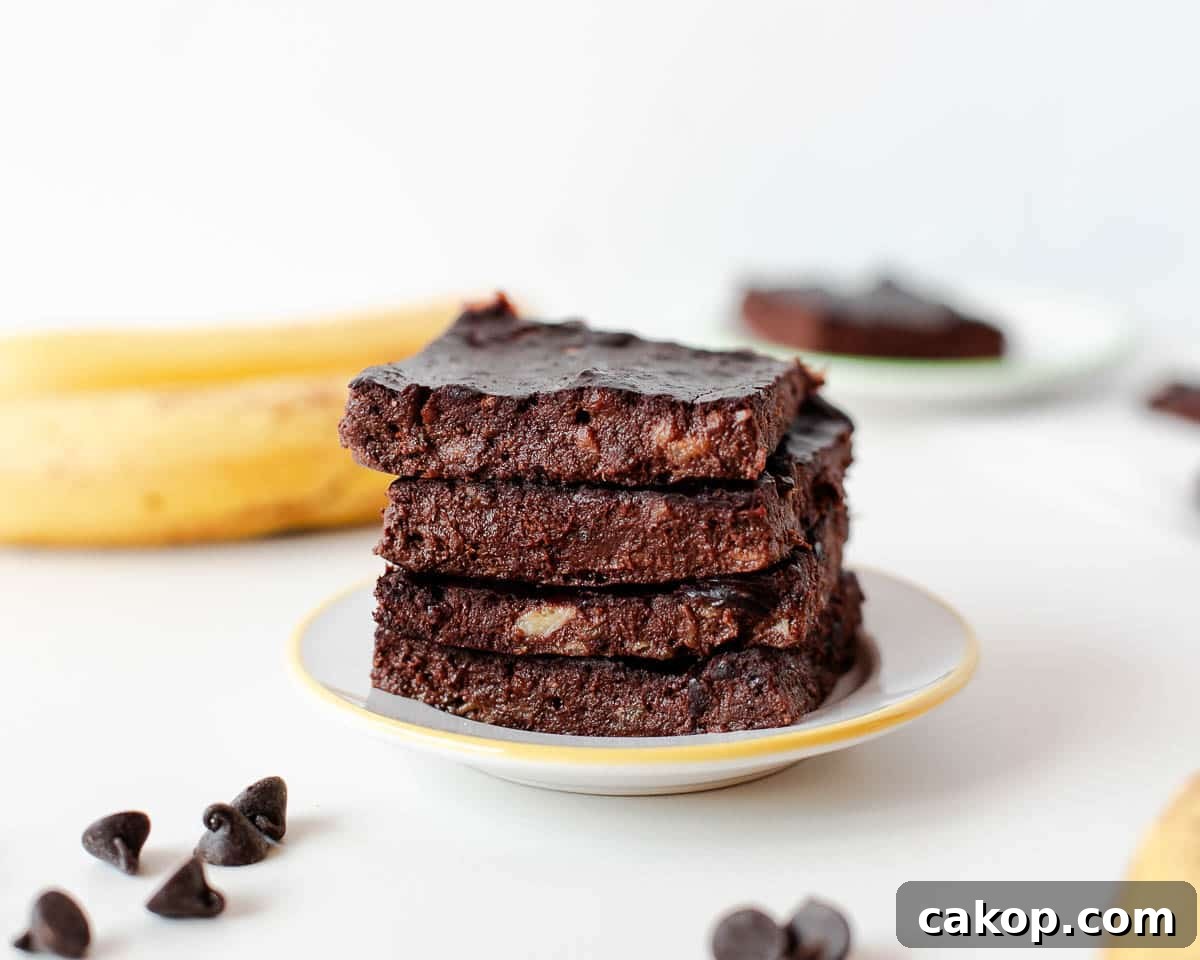 Stack of fudgy 3 ingredient banana brownies on a small plate with chocolate chips and banana in background.