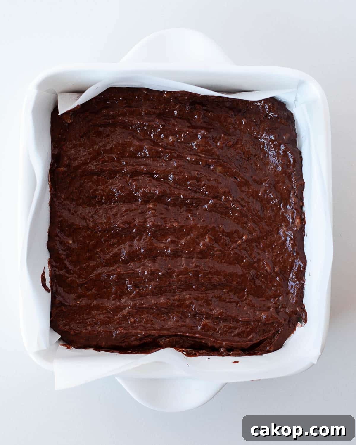 Chocolate banana brownie batter spread evenly in an 8x8 parchment-lined baking dish before baking.