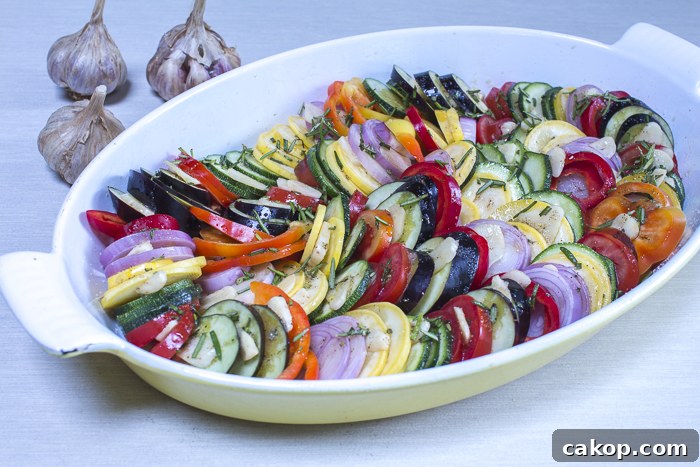 The vegetables layered in an oval baking dish ready to roast in the oven
