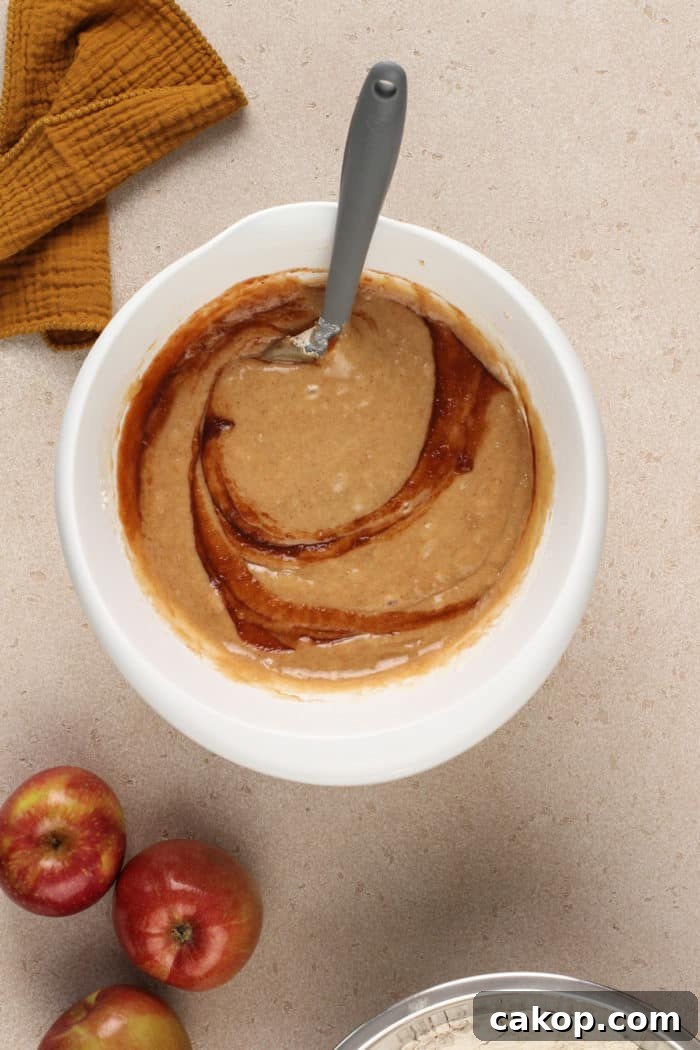Apple butter being folded into cake batter in a white mixing bowl.