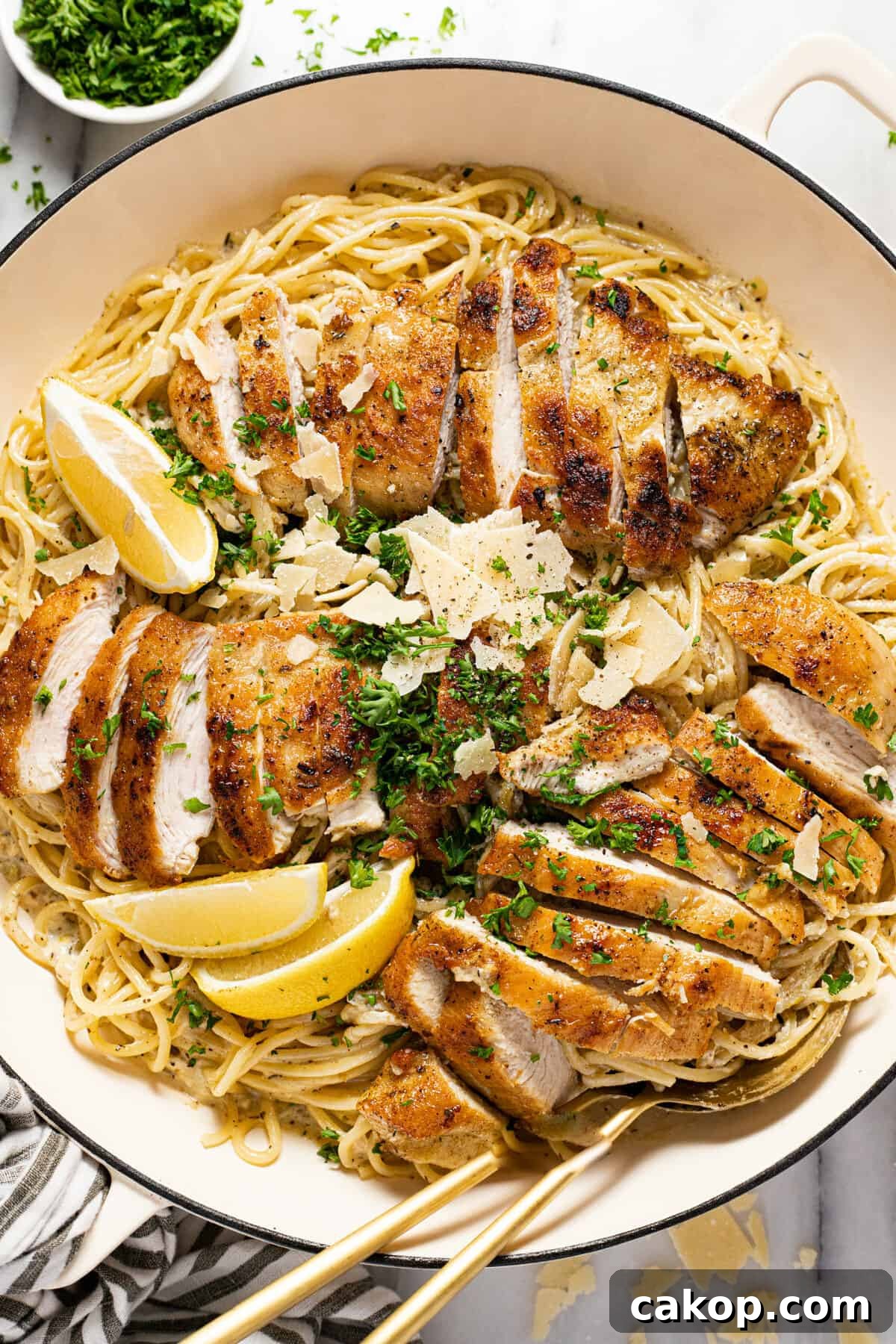 Large white pan filled with creamy spaghetti and sliced lemon chicken garnished with parsley.