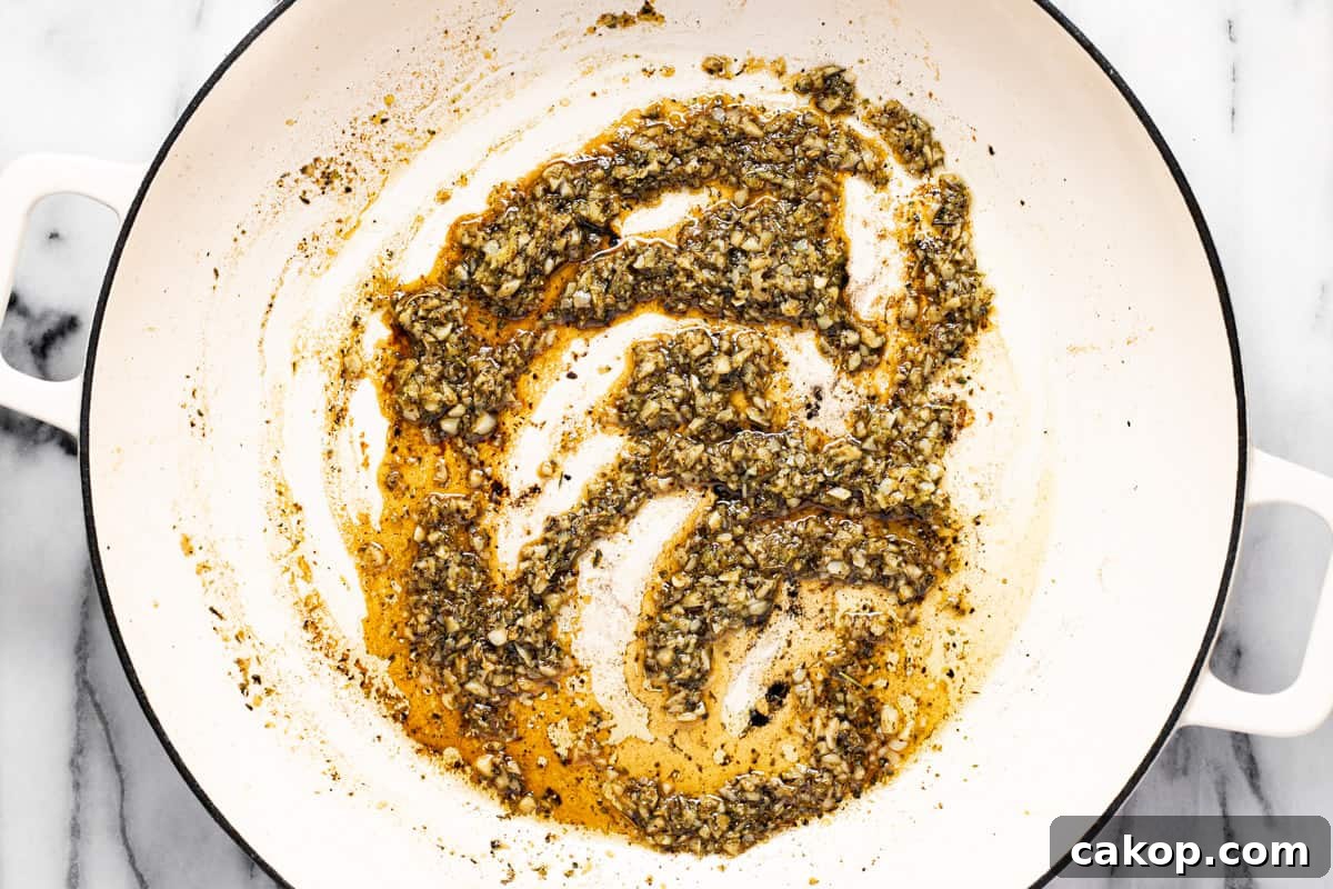 Sauteed garlic, herbs, and spices in olive oil in a large white pan.