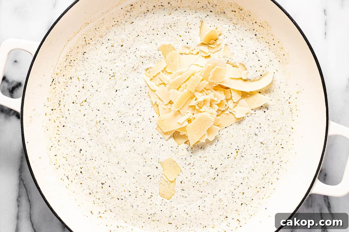 Large white pan filled with lemon cream sauce with Parmesan cheese being added.