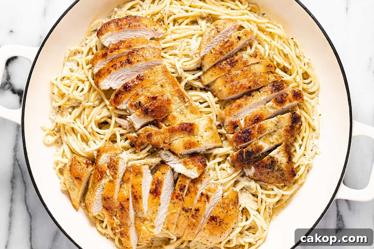 Creamy lemon spaghetti with sliced lemon chicken in a large white pan.
