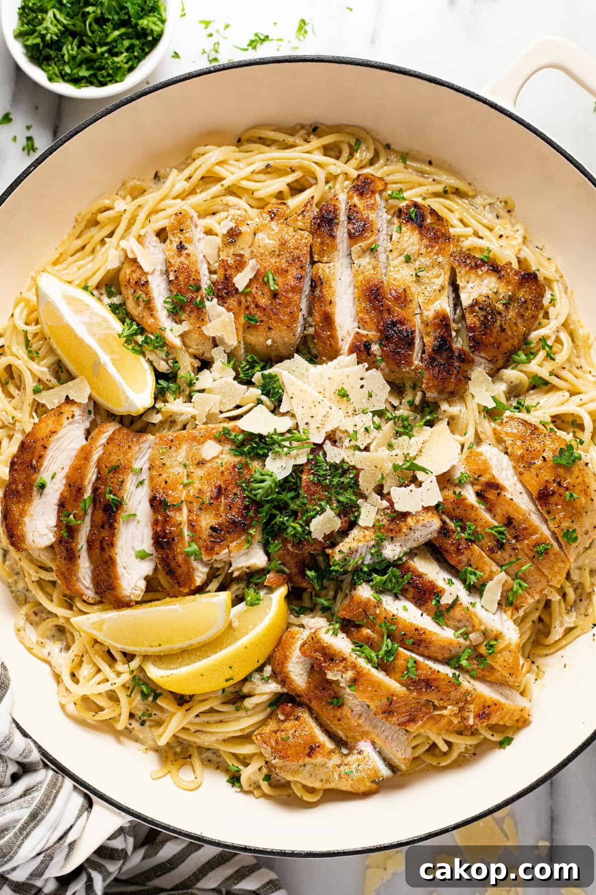 Large white pan filled with creamy spaghetti and sliced lemon chicken garnished with parsley.