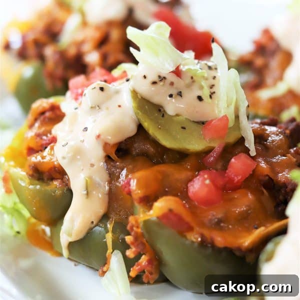 Square image closeup of cheeseburger stuffed peppers on a white plate, topped with lettuce, tomato, pickle, and Copycat Big Mac Sauce