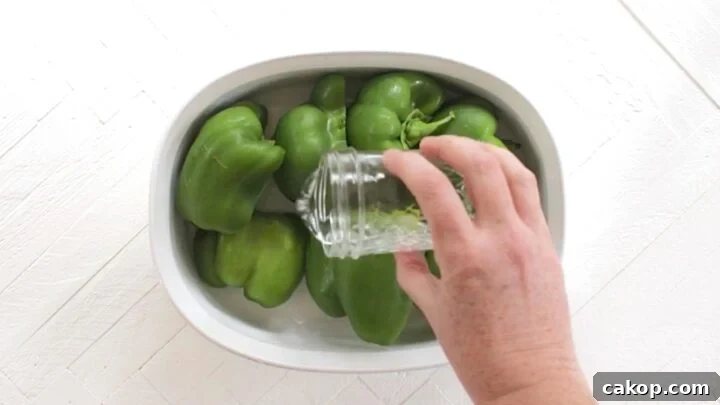 Adding water to halved bell peppers in a white oval dish.