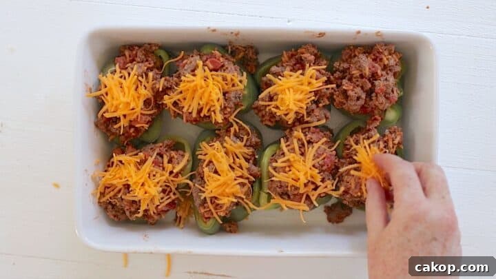 Stuffed peppers with cheeseburger filling topped with shredded cheese ready for baking.