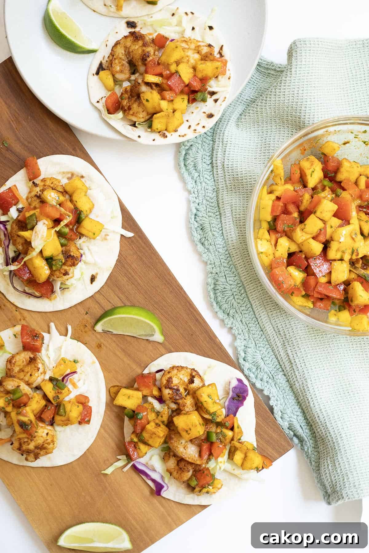 Mango-Lime Shrimp Tacos with Fresh Cilantro Salsa 2 three shrimp tacos on white flour tortillas topped with mango salsa with a lime wedge in the middle.