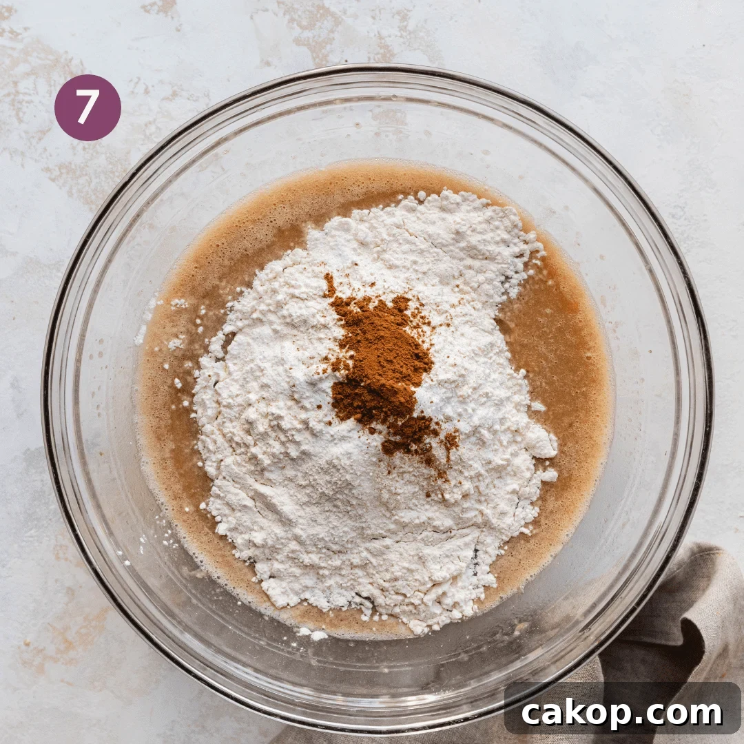 flour, salt, and spices sitting on top of liquid ingredients for vegan banana bread in a glass bowl.