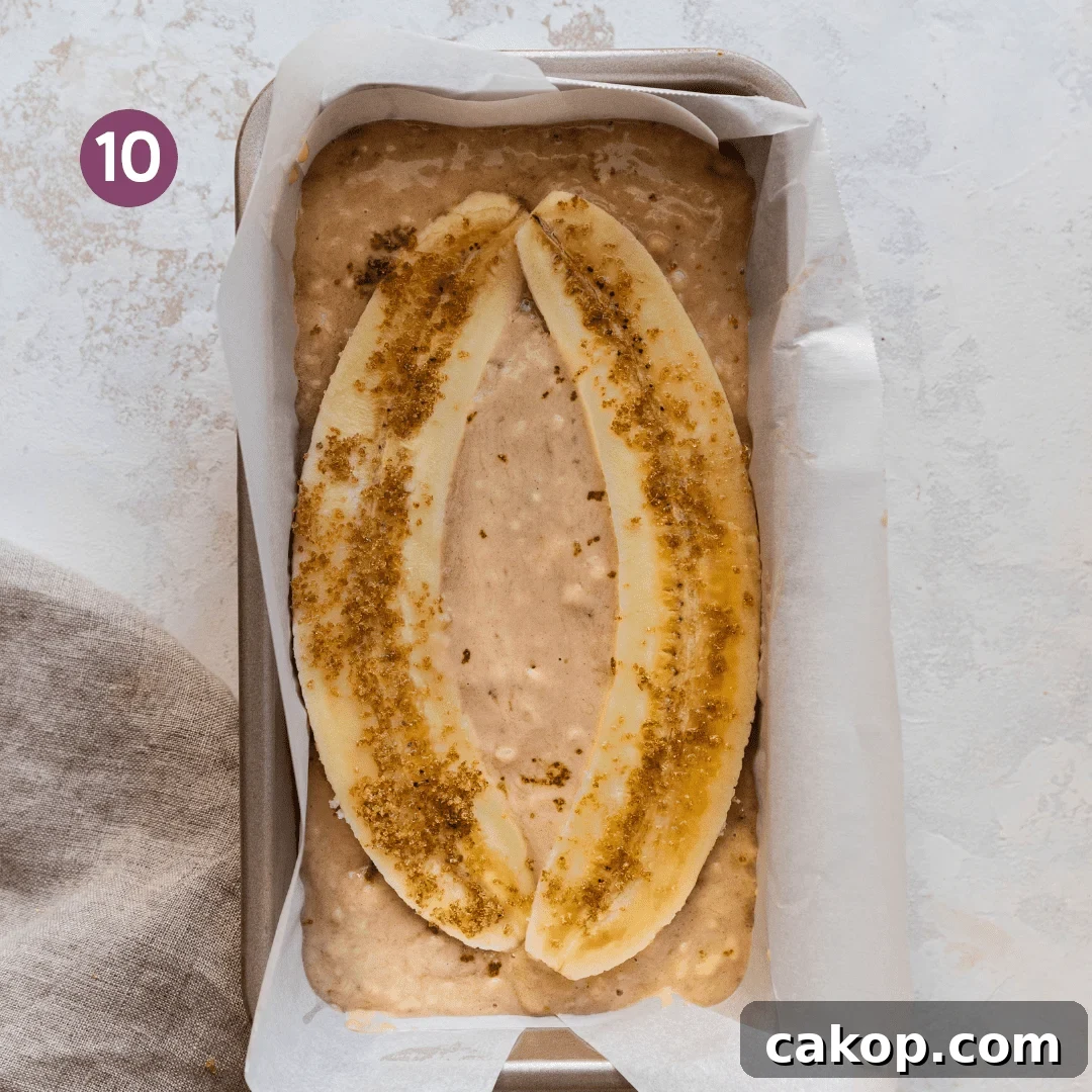 vegan banana bread batter in a parchment paper loaf pan with sliced bananas on top.