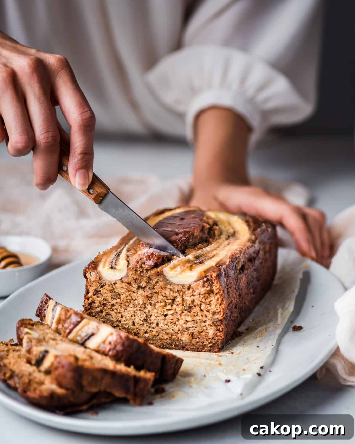 woman's hands slicing into a beautiful vegan banana bread on a platter.
