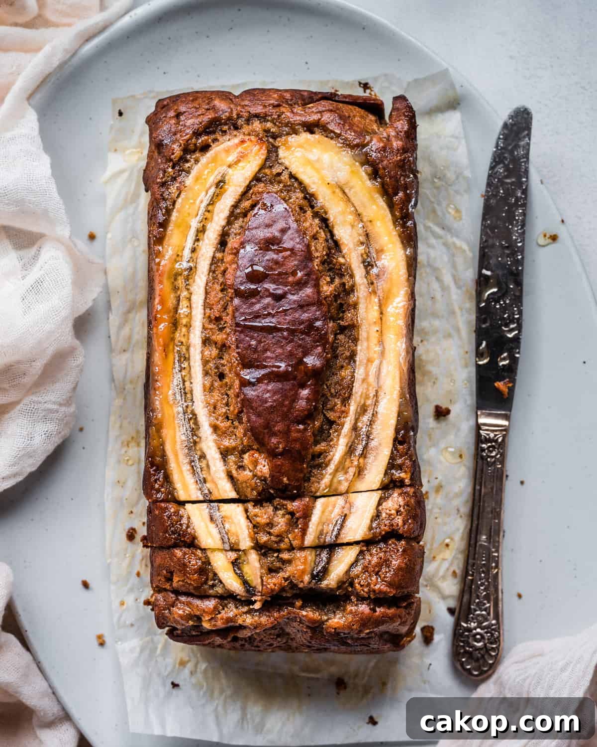 overhead shot of a beautiful vegan banana bread with a banana slice baked into the top, drizzled with honey, on a platter.