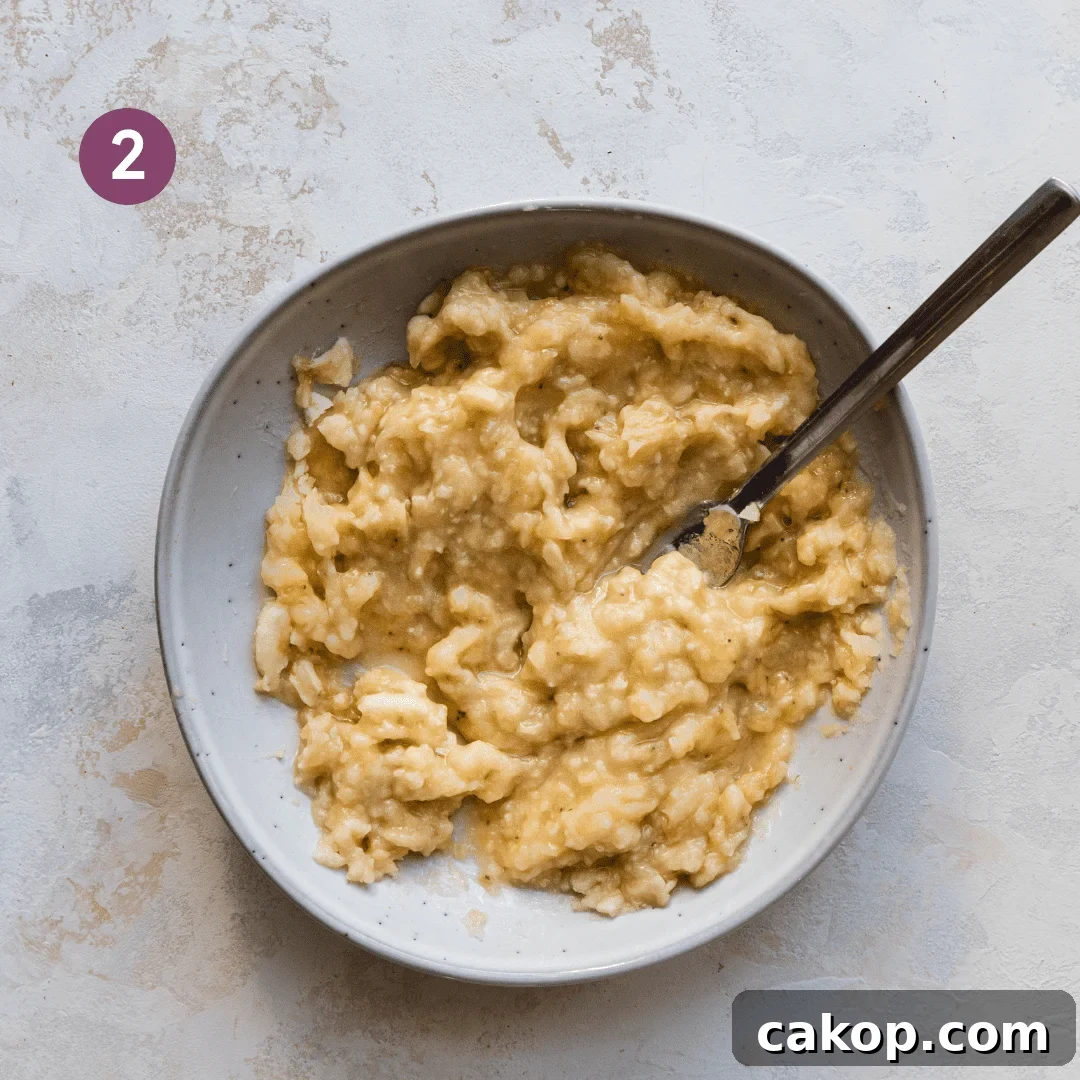 mashed bananas in a ceramic bowl with a fork in the bowl.