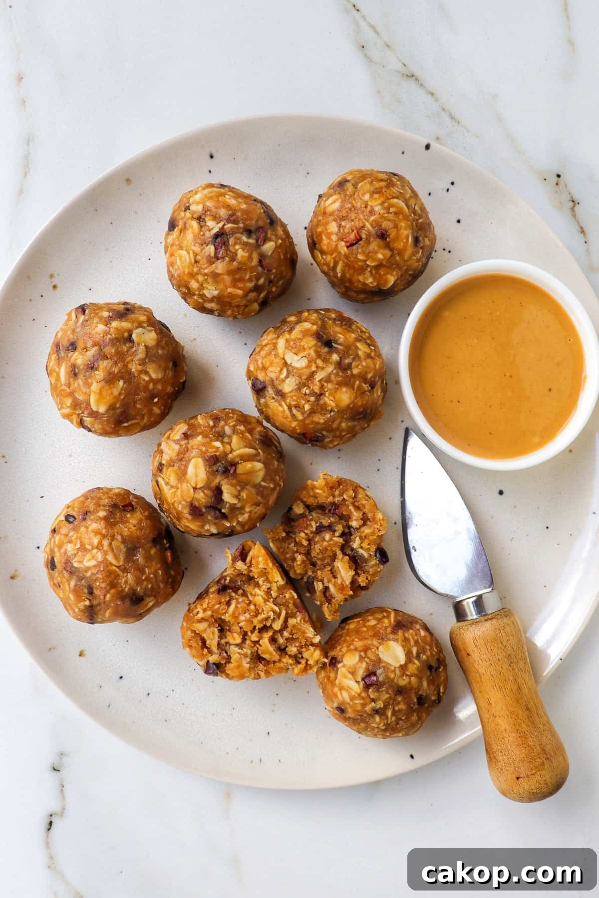 Bliss balls on a plate with a knife and dish of peanut butter. One cut in half.