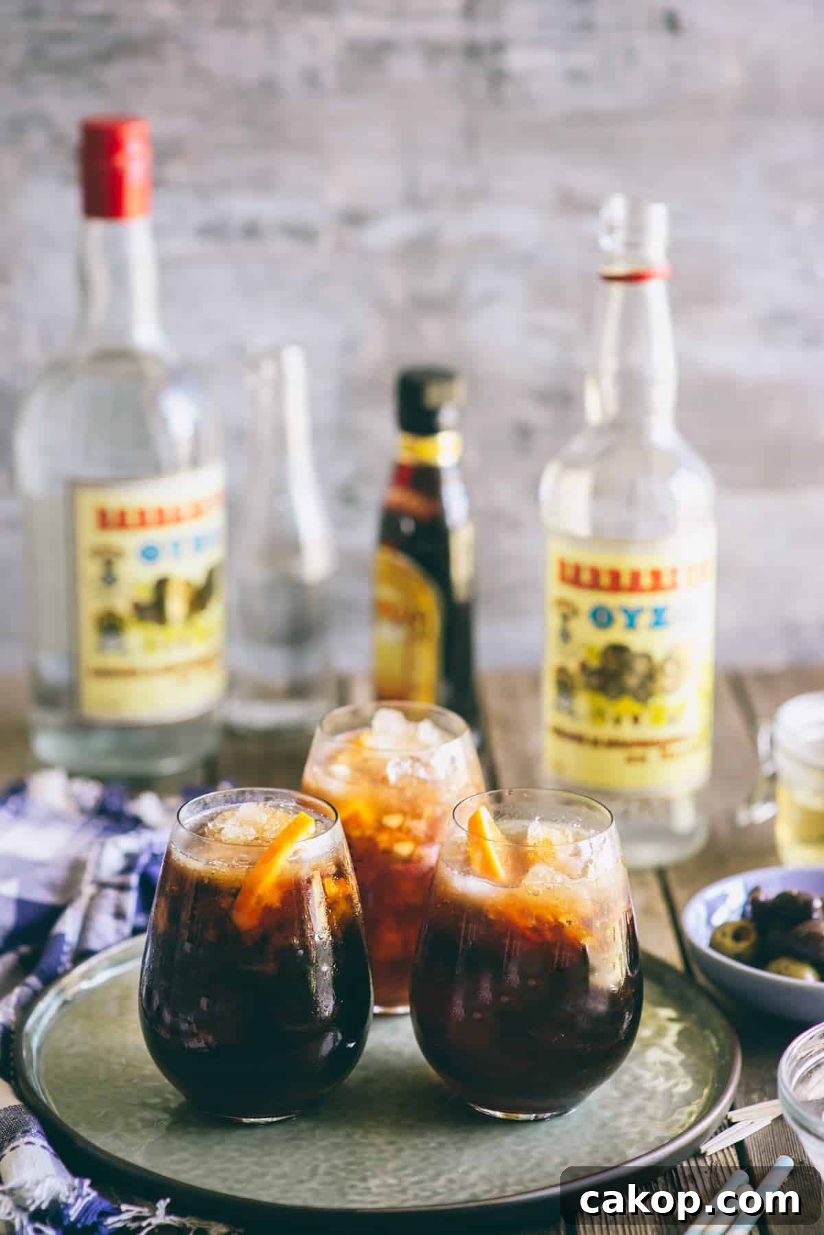 Ouzo coffee cocktails served over ice with orange garnish on a tray with Greek spirits in the background.