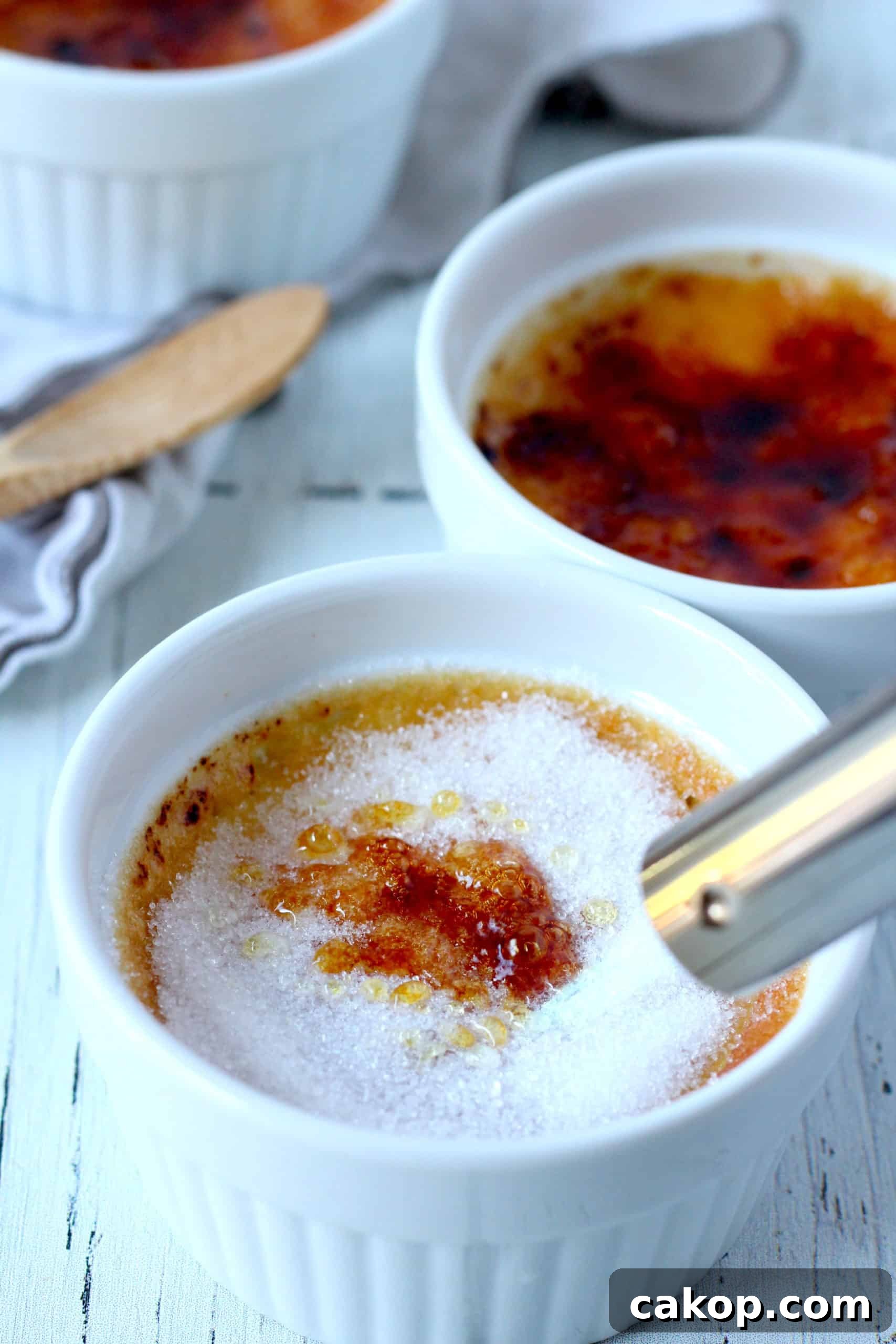 creamy creme brule in white ramekin with sugar being melted by torch another ramekin with creme brulee in background