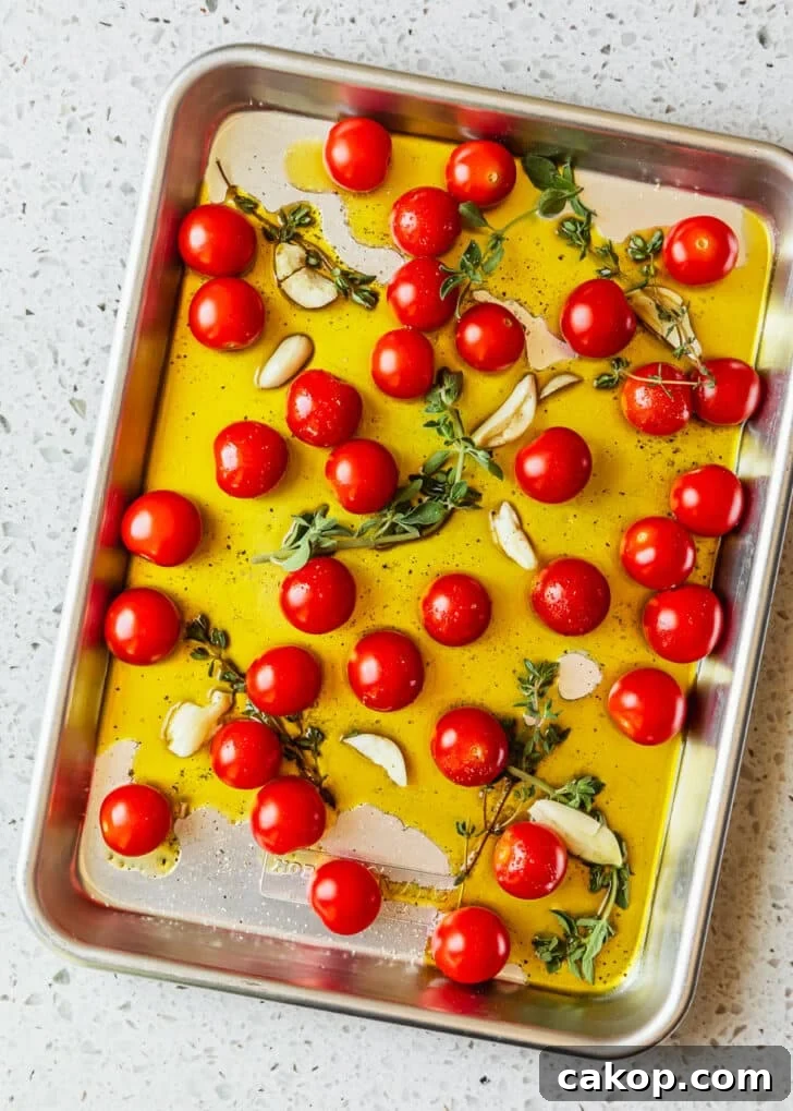 A sheet pan of tomatoes, oil, and herbs on a white terrazzo counter.